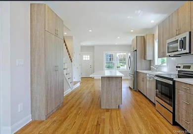 Kitchen with stainless steel appliances, a center island, modern cabinets, light countertops, and light wood finished floors