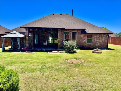 Back of property featuring brick siding, a gazebo, a patio, roof with shingles, and a fire pit