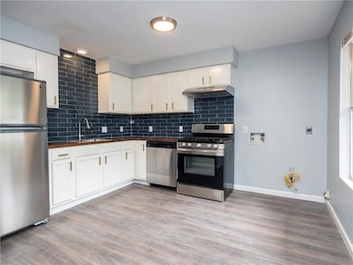 Kitchen with backsplash, appliances with stainless steel finishes, and white cabinets
