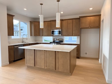 Kitchen with brown cabinets, a kitchen island, stainless steel appliances, hanging light fixtures, and light stone counters