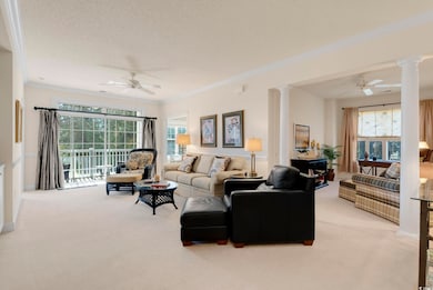 Living area featuring light carpet, a ceiling fan, and decorative columns