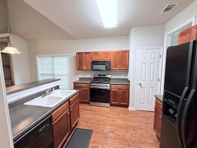 Kitchen with black appliances, a sink, dark countertops, brown cabinets, and light wood finished floors