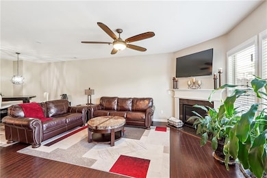 Living room with a glass covered fireplace, wood-type flooring, ceiling fan, and baseboards