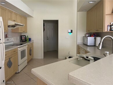 Kitchen with decorative backsplash, white appliances, light brown cabinets, and light tile patterned floors
