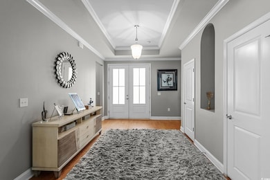 Entrance foyer featuring french doors, a raised ceiling, ornamental molding, and wood finished floors