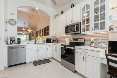 Kitchen with appliances with stainless steel finishes, decorative backsplash, glass insert cabinets, arched walkways, and light tile patterned floors