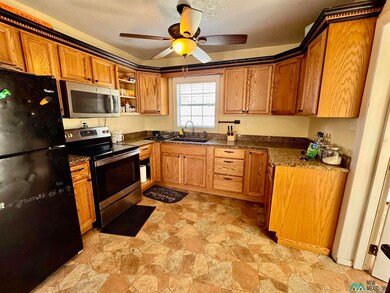 Kitchen with stainless steel appliances, stone finish flooring, ceiling fan, open shelves, and dark stone counters