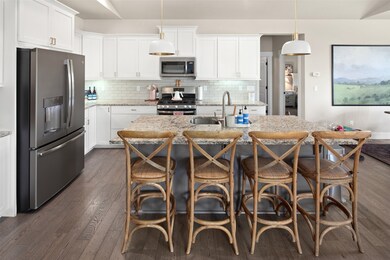 Kitchen featuring appliances with stainless steel finishes, backsplash, white cabinets, light stone counters, and a kitchen island with sink