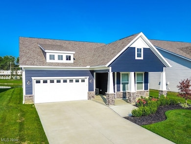 View of front facade featuring driveway, a front yard, a shingled roof, stone siding, and covered porch