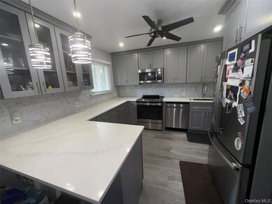 Kitchen with appliances with stainless steel finishes, gray cabinets, a peninsula, decorative backsplash, and dark wood-style flooring