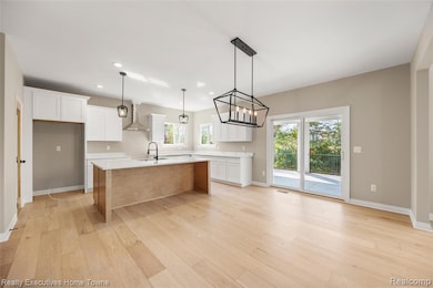 Kitchen featuring white cabinetry, light wood-style flooring, wall chimney exhaust hood, hanging light fixtures, and recessed lighting