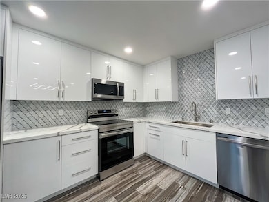 Kitchen with modern cabinets, appliances with stainless steel finishes, white cabinetry, light stone countertops, and decorative backsplash