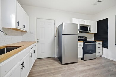 Kitchen featuring butcher block counters, stainless steel appliances, white cabinetry, light wood-style floors, and backsplash