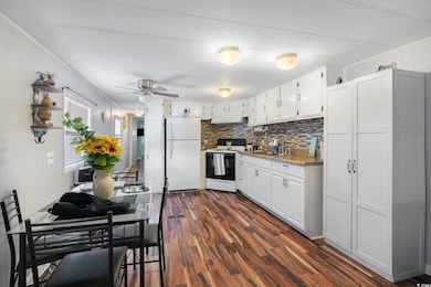 Kitchen featuring white cabinetry, freestanding refrigerator, electric stove, dark wood-style floors, and tasteful backsplash
