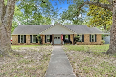 Ranch-style house with covered porch, brick siding, roof with shingles, and a front lawn