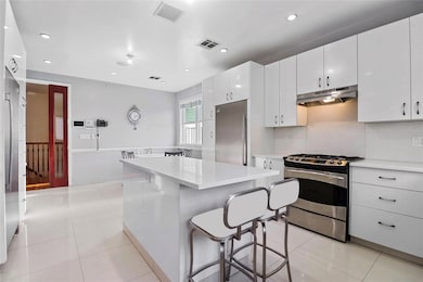 Kitchen with appliances with stainless steel finishes, a breakfast bar area, under cabinet range hood, light countertops, and light tile patterned floors