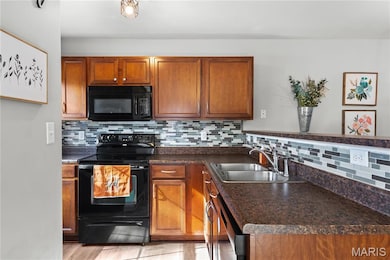 Kitchen featuring black appliances, decorative backsplash, dark countertops, and brown cabinets
