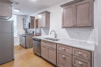 Kitchen with appliances with stainless steel finishes, a sink, light stone counters, tasteful backsplash, and baseboards