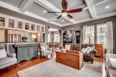 Living area with light wood-style floors, coffered ceiling, beamed ceiling, and ceiling fan with notable chandelier