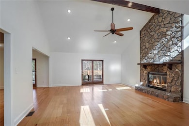 Unfurnished living room with beam ceiling, a stone fireplace, high vaulted ceiling, and light hardwood / wood-style floors