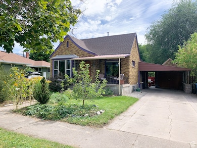 View of front of home featuring brick siding, driveway, an attached carport, roof with shingles, and a front yard