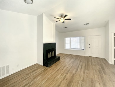 Unfurnished living room featuring a textured ceiling, lofted ceiling, light wood finished floors, a brick fireplace, and ceiling fan