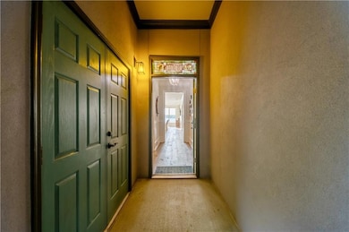 Doorway featuring a textured wall, crown molding, and light colored carpet