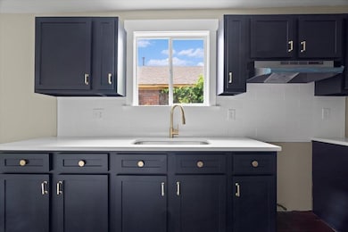Kitchen with a sink, under cabinet range hood, backsplash, and light countertops