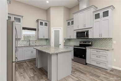 Kitchen with stainless steel appliances, glass insert cabinets, a kitchen island, light wood-type flooring, and a high ceiling
