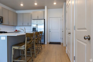 Kitchen with gray cabinets, appliances with stainless steel finishes, light wood-style floors, recessed lighting, and a center island with sink