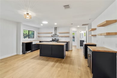 Kitchen with dark cabinets, open shelves, recessed lighting, a kitchen island, and light wood-style flooring