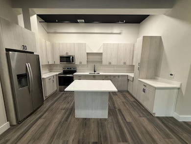 Kitchen featuring appliances with stainless steel finishes, a sink, a center island, open shelves, and dark wood-style flooring
