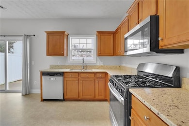 Kitchen with appliances with stainless steel finishes, light stone counters, brown cabinets, and a textured ceiling