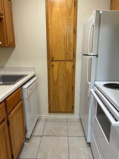 Kitchen with light tile patterned floors, light countertops, stove, brown cabinetry, and dishwashing machine