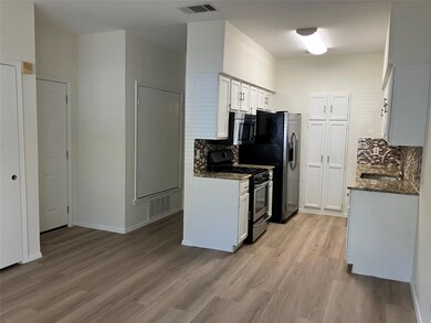 Kitchen with dark stone countertops, stainless steel appliances, white cabinetry, light wood-type flooring, and backsplash