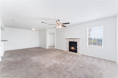 Unfurnished living room featuring a stone fireplace, a textured ceiling, carpet floors, and ceiling fan