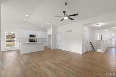 Unfurnished living room featuring healthy amount of natural light, light wood-style flooring, vaulted ceiling, ceiling fan, and recessed lighting