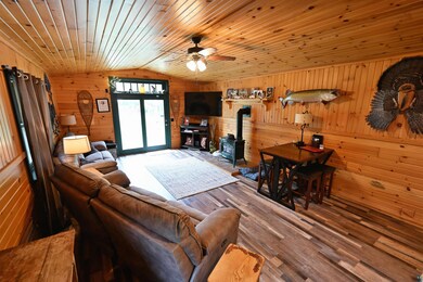 Living area with lofted ceiling, wood walls, a wood stove, a ceiling fan, and wood finished floors