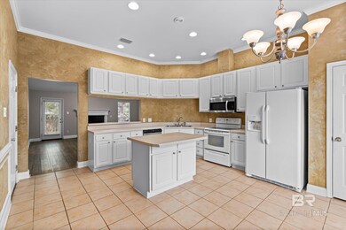 Kitchen featuring ornamental molding, appliances with stainless steel finishes, hanging light fixtures, and white cabinetry