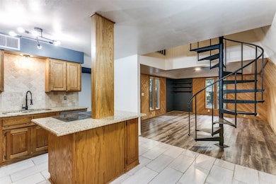 Kitchen featuring tasteful backsplash, light stone countertops, light wood-style flooring, brown cabinetry, and a kitchen island