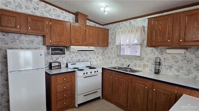 Kitchen featuring white appliances, wallpapered walls, ornamental molding, a textured ceiling, and brown cabinetry