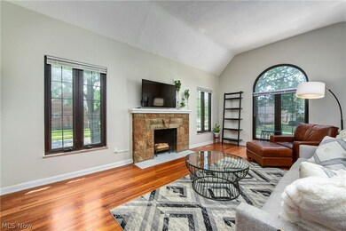 Living room with a stone fireplace, hardwood floors, and vaulted ceiling