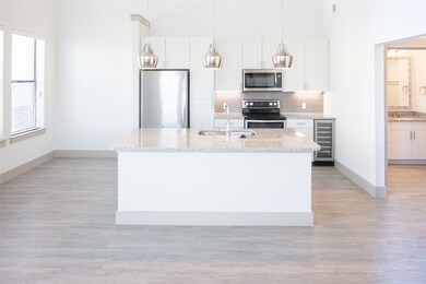 Kitchen with light stone countertops, white cabinetry, wine cooler, a kitchen island with sink, and appliances with stainless steel finishes
