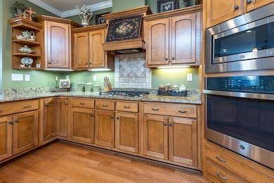 Kitchen with ornamental molding, stainless steel appliances, brown cabinets, light stone countertops, and open shelves