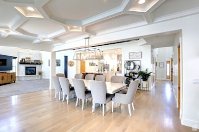 Dining space with coffered ceiling, a fireplace, light wood-style floors, a chandelier, and beam ceiling
