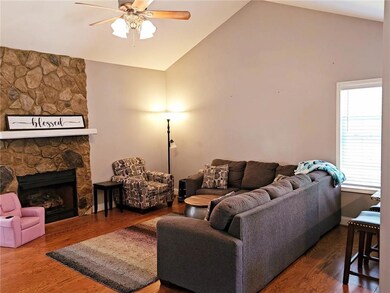 Living room with ceiling fan, lofted ceiling, a stone fireplace, and wood finished floors