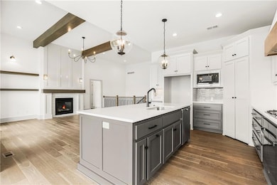 Kitchen featuring light countertops, white cabinets, a sink, an island with sink, and black microwave
