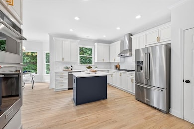 Kitchen featuring appliances with stainless steel finishes, white cabinetry, backsplash, light wood-style flooring, and crown molding