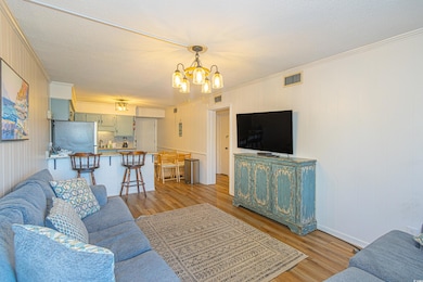 Living area featuring visible vents, an inviting chandelier, crown molding, and light wood finished floors
