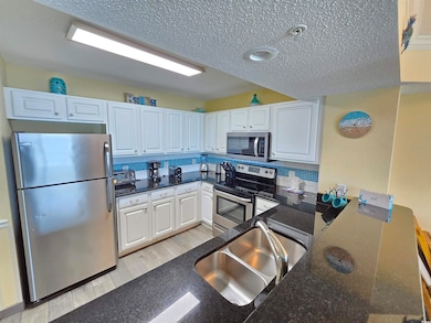 Kitchen featuring appliances with stainless steel finishes, white cabinets, a textured ceiling, backsplash, and light wood-style floors
